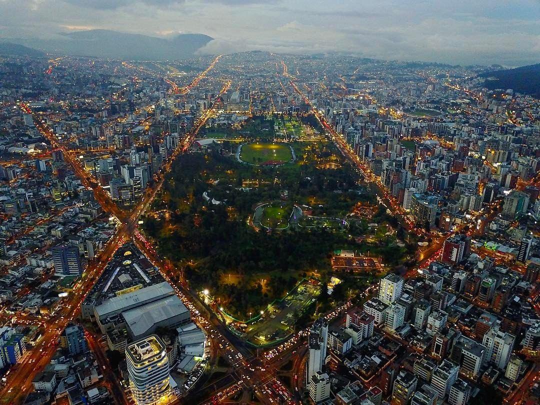 Vista aérea de un parque de Quito al anochecer, rodeado de edificios